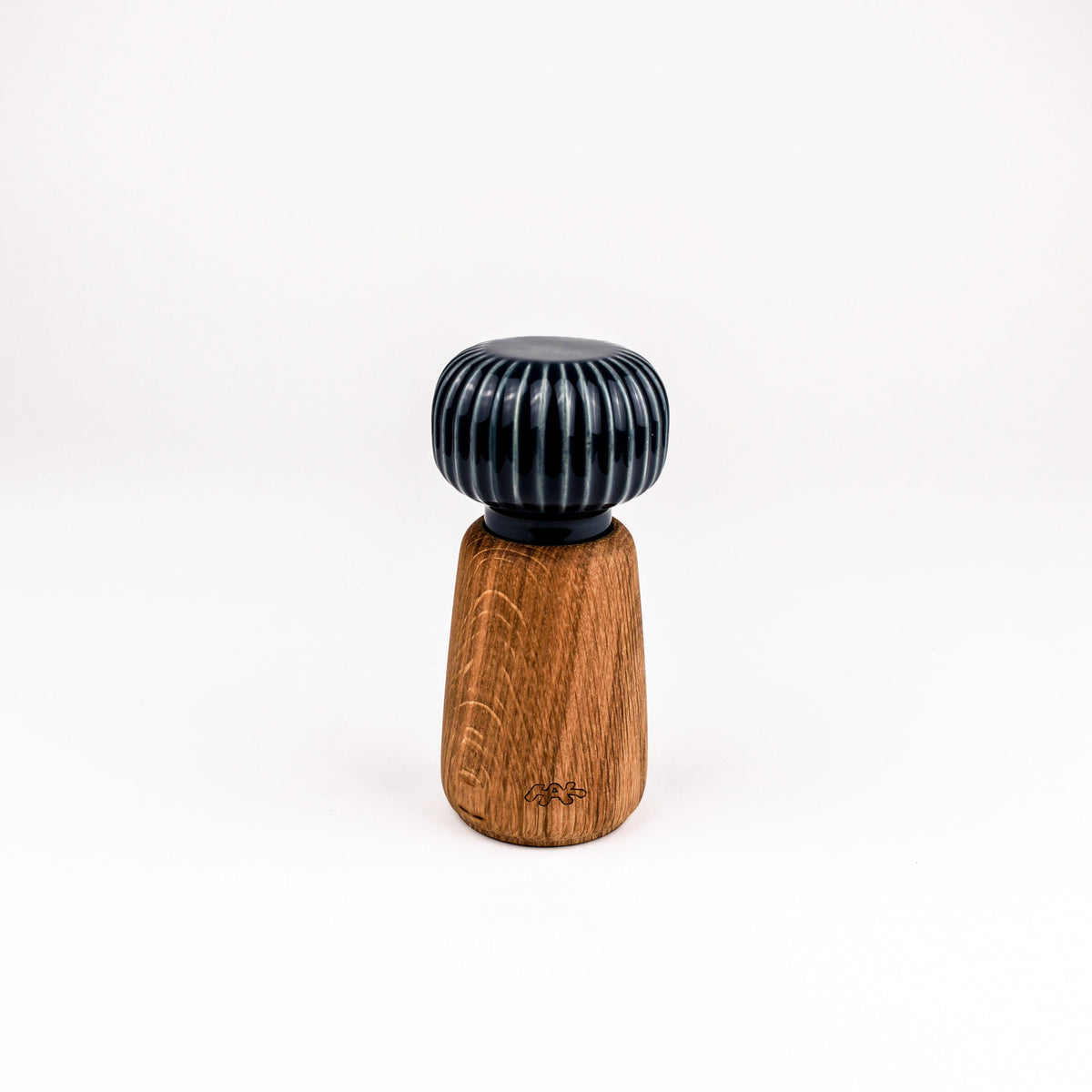 A small decorative object with a dark blue-green ribbed top and a tapered brown wooden base, centered on a plain white studio background.