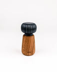 A small decorative object with a dark blue-green ribbed top and a tapered brown wooden base, centered on a plain white studio background.