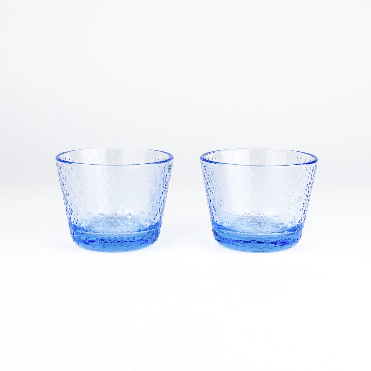 Two small textured blue glass tumblers with a hammered pattern, shown side by side on a clean white background.