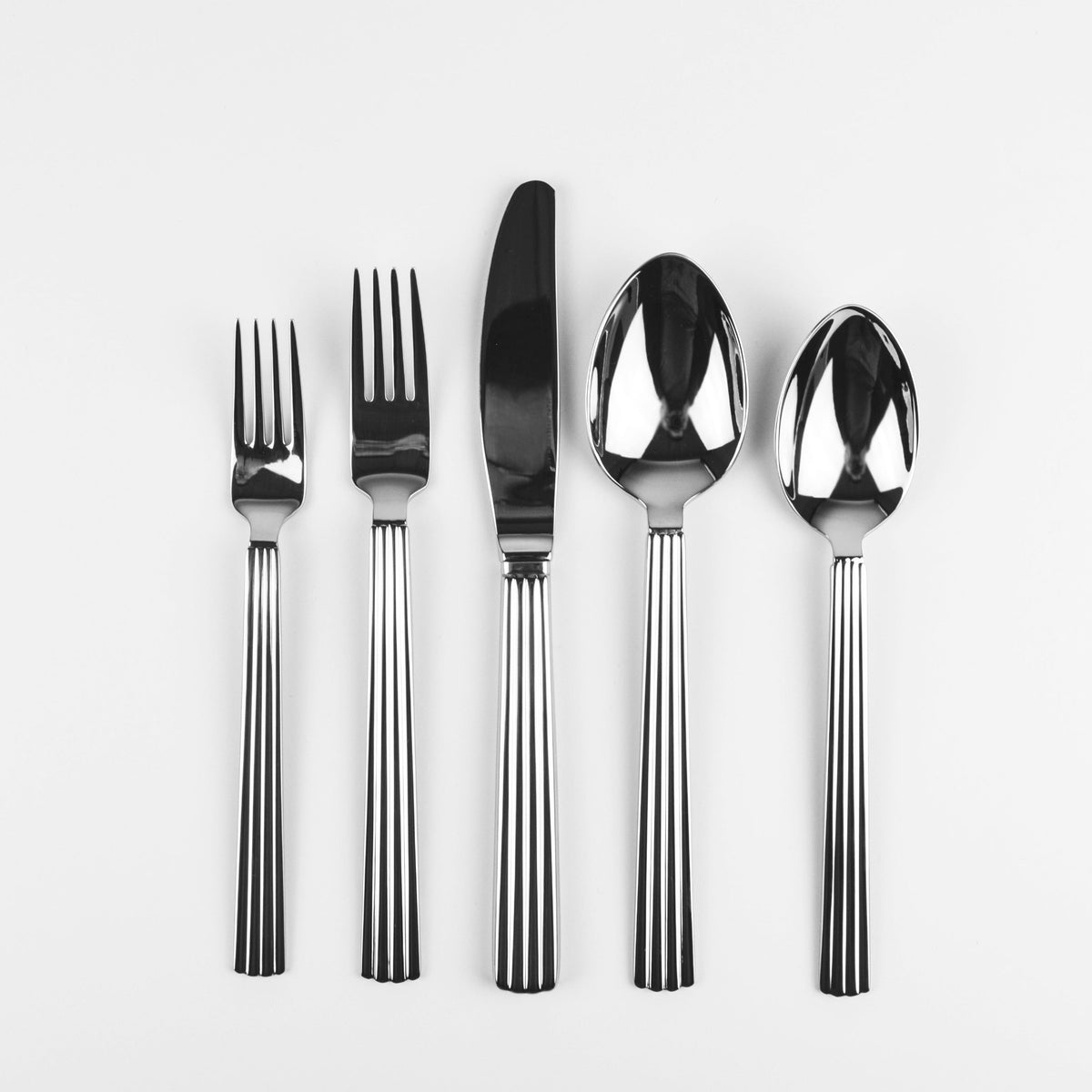Five-piece stainless steel cutlery set with a fork, knife, and two spoons, aligned vertically on a plain white background.