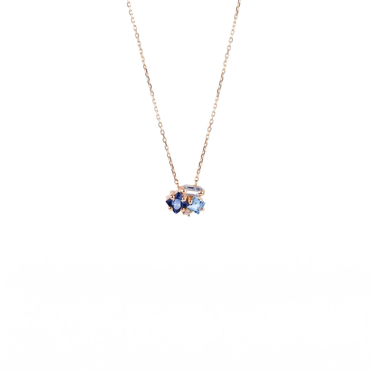 A delicate yellow gold chain necklace with a small cluster pendant featuring dark blue and light blue gemstones, set against a solid white background.