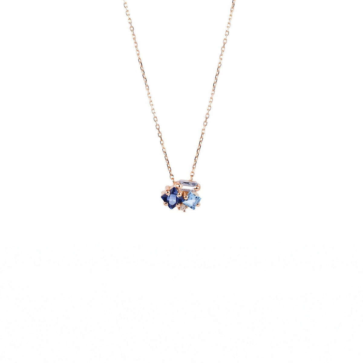 A delicate yellow gold chain necklace with a small cluster pendant featuring dark blue and light blue gemstones, set against a solid white background.