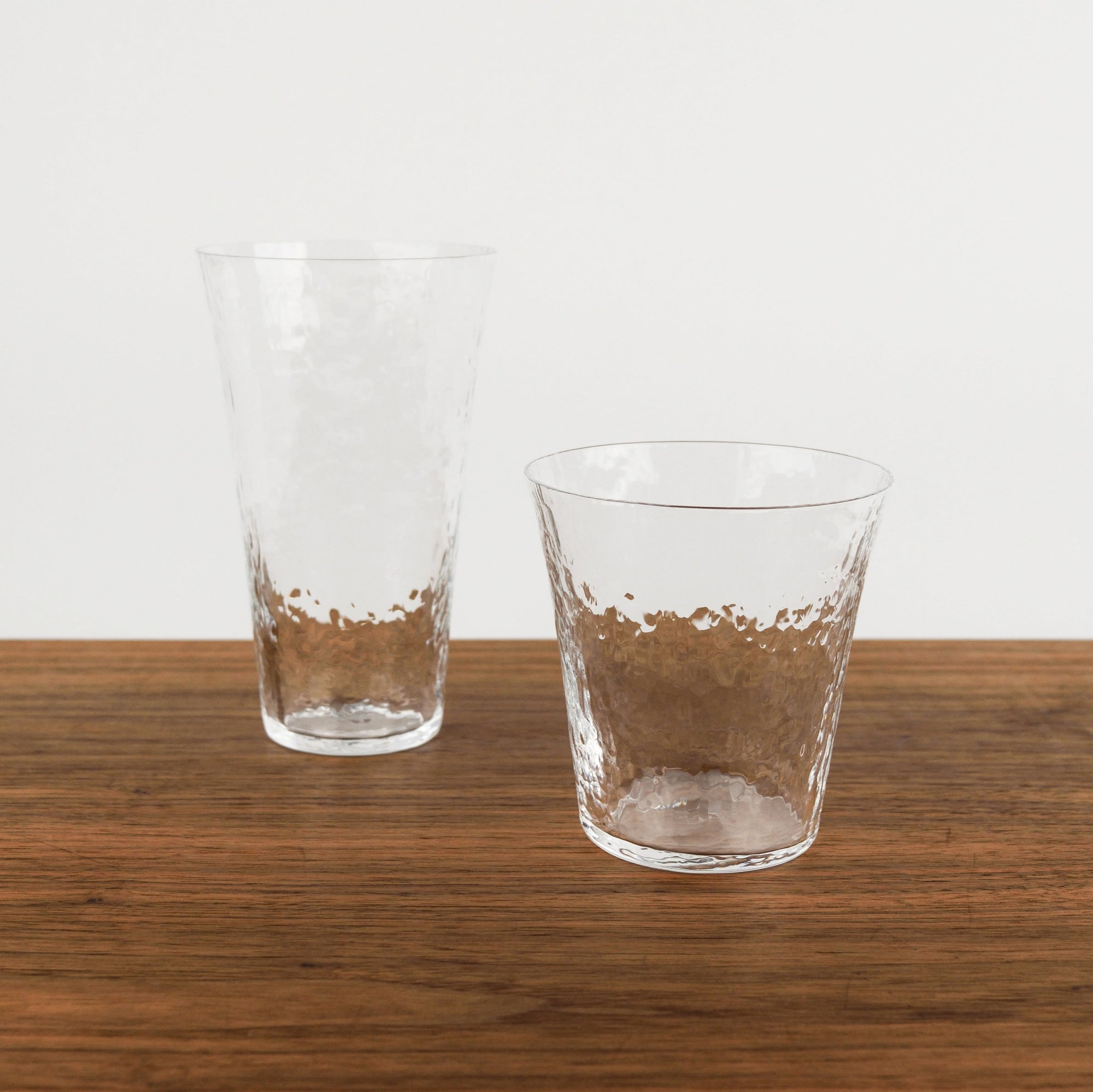 Two clear glass tumblers on a wooden surface with a white background