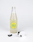 A clear glass bottle of Boylan Sparkling Lemonade with a yellow label stands on a white studio background, alongside a silver bottle opener and a black bottle cap.