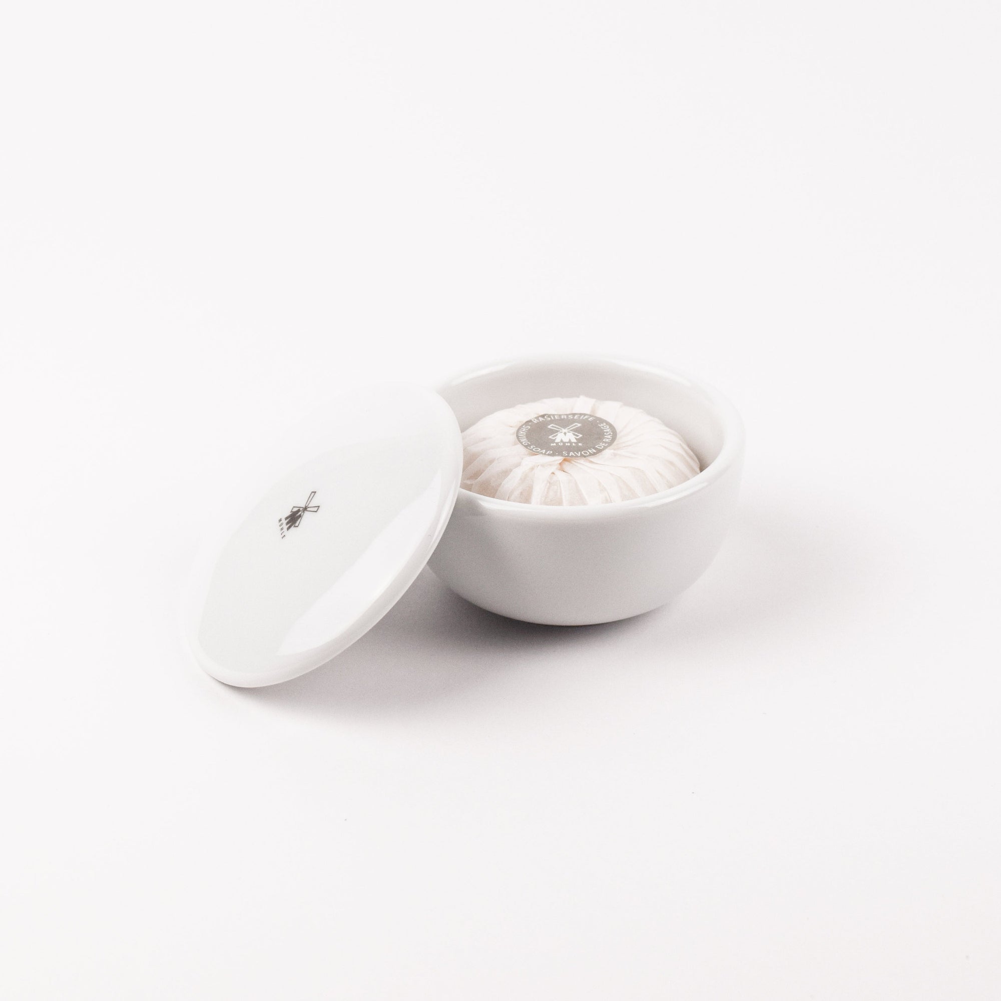 White ceramic bowl with lid and shaving soap on a white background