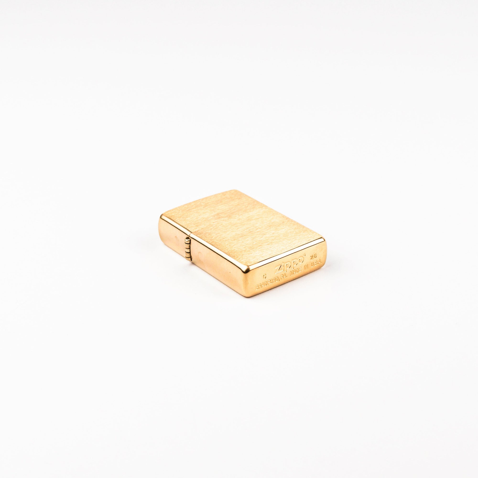 A small rectangular gold-toned metal lighter with a brushed finish and engraved markings, photographed on a clean white background.