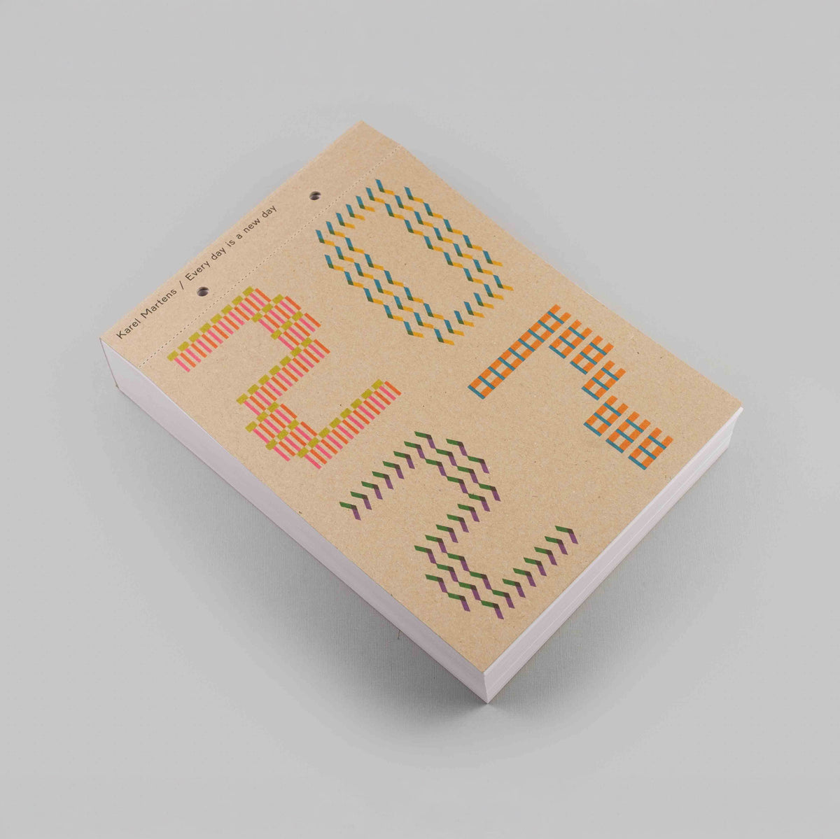 A notebook with a kraft paper cover featuring colorful geometric patterns, photographed at an angle on a neutral gray background.