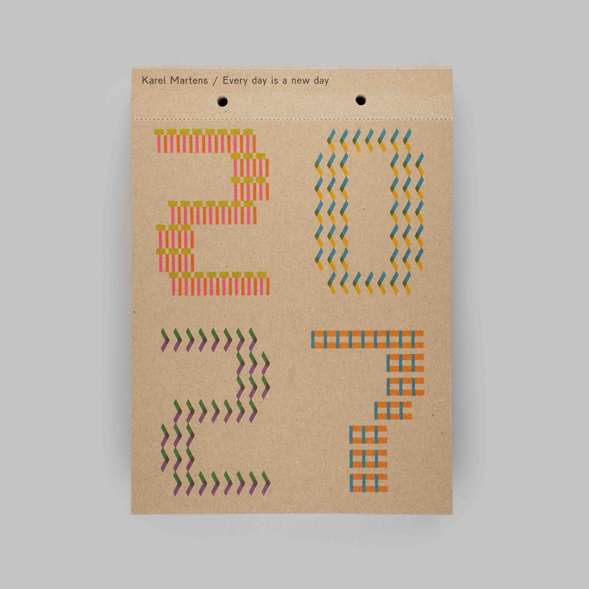 A kraft paper hanging card with the text 'Kani Martens / Every day is a new day' at the top, featuring colorful geometric arrow patterns arranged to spell out '2027' on a plain light gray background.