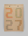 A kraft paper hanging card with the text 'Kani Martens / Every day is a new day' at the top, featuring colorful geometric arrow patterns arranged to spell out '2027' on a plain light gray background.