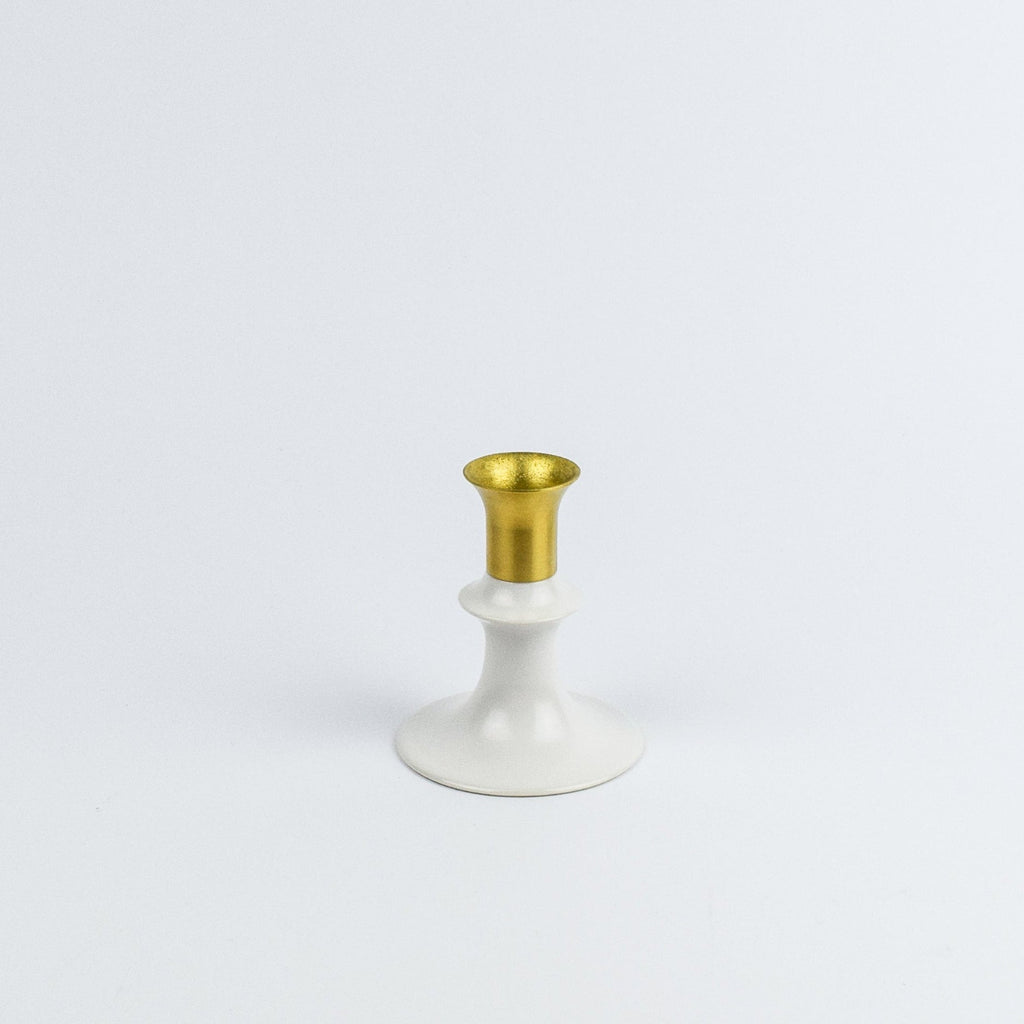 Decorative candle holder with gold top and white base on a light gray background