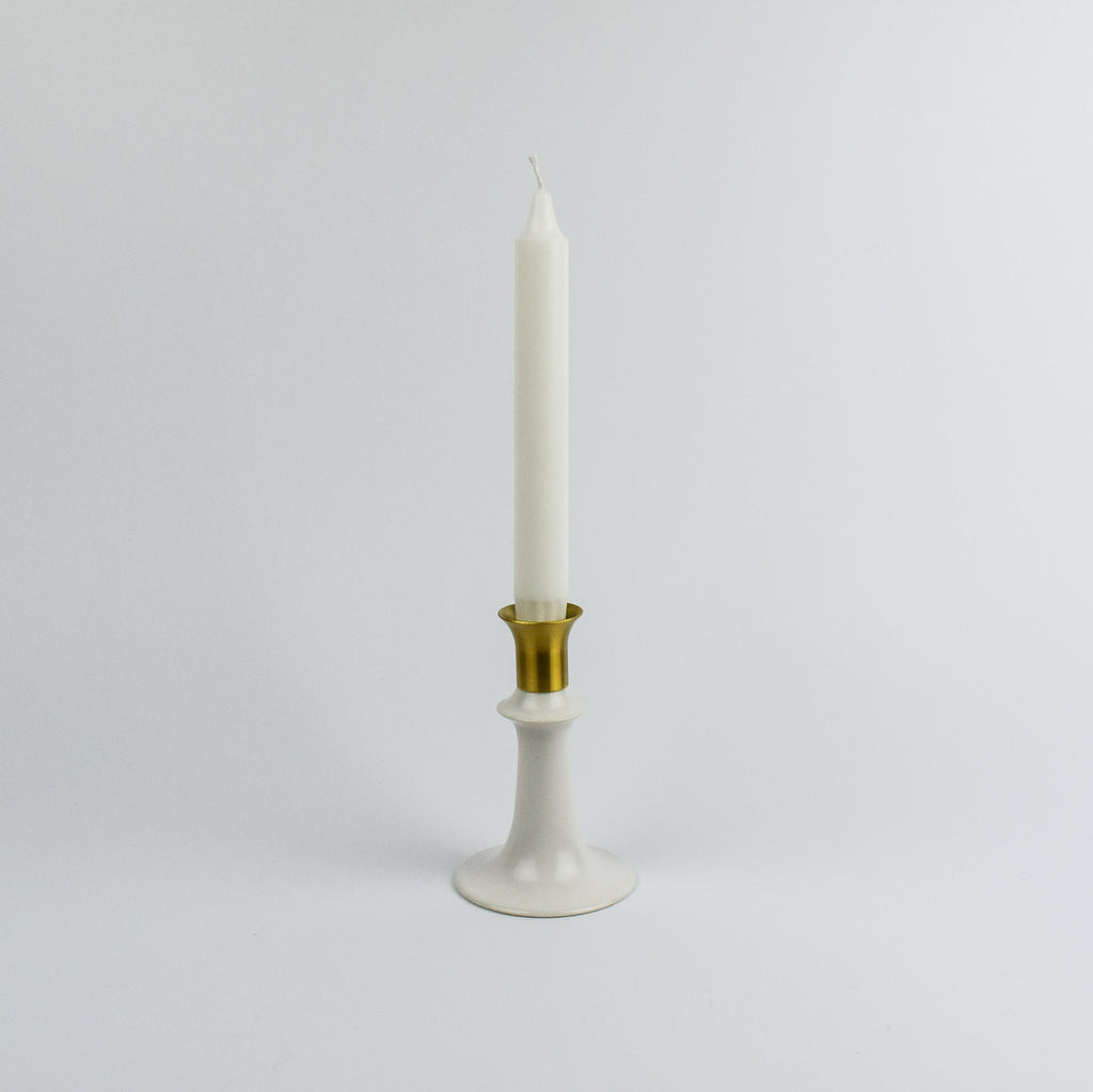 White candle in a gold and white holder on a light gray background