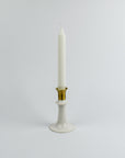 White candle in a gold and white holder on a light gray background