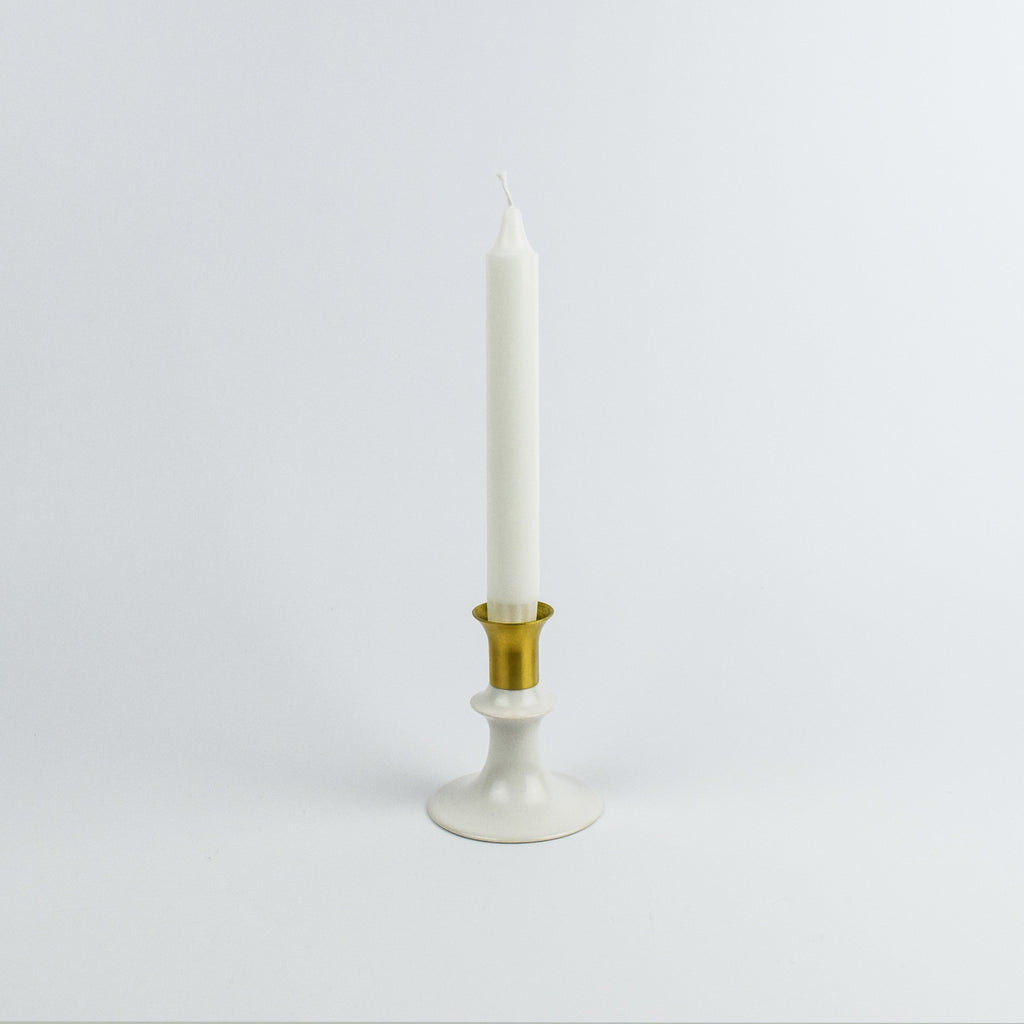 White candle in a gold and white holder on a light gray background