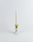 White candle in a gold and white holder on a light gray background