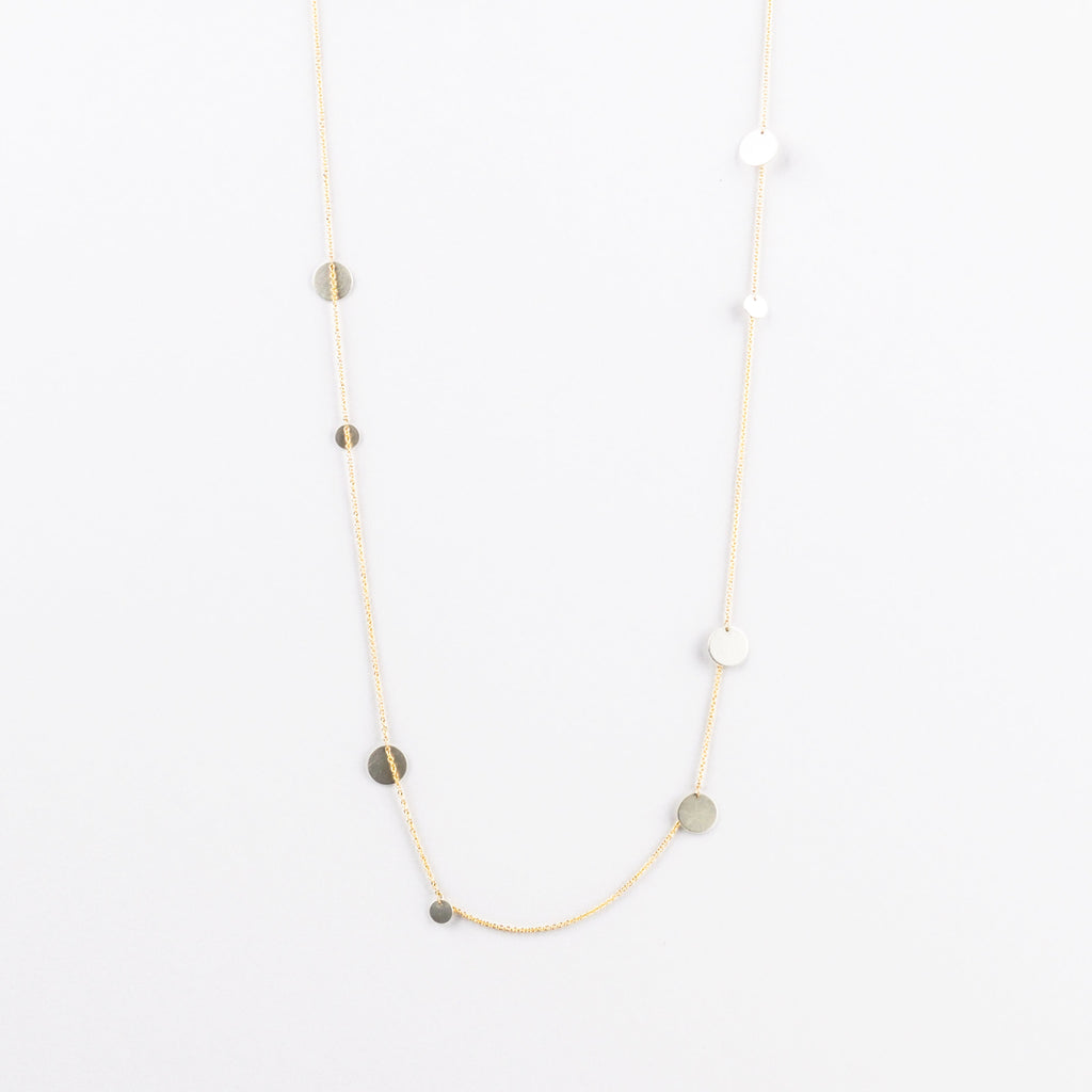 Gold chain necklace with small round silver discs  on a light gray background