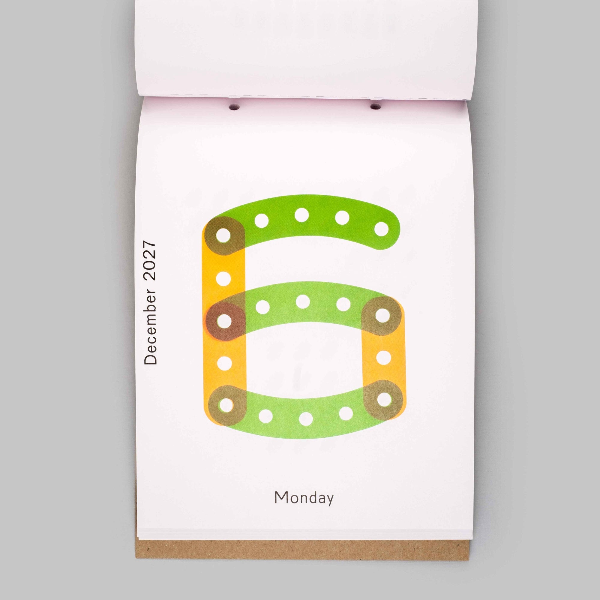 A top-down view of a hanging desk calendar page showing the number 6 in green and orange with the date December 2021 and the day Monday on a white page, set against a solid gray background.