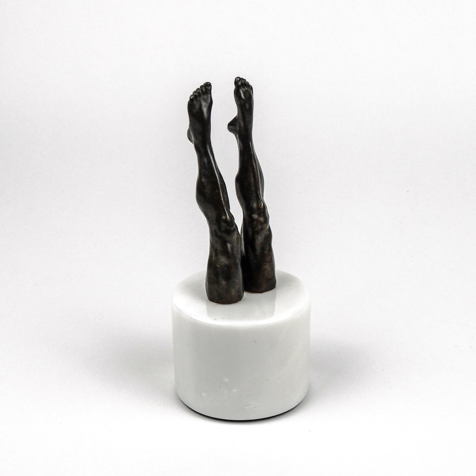 Bronze sculpture of legs on a white marble base against a white background