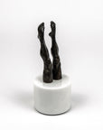 Bronze sculpture of legs on a white marble base against a white background