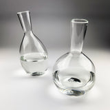 Two clear glass decanters on a gray background