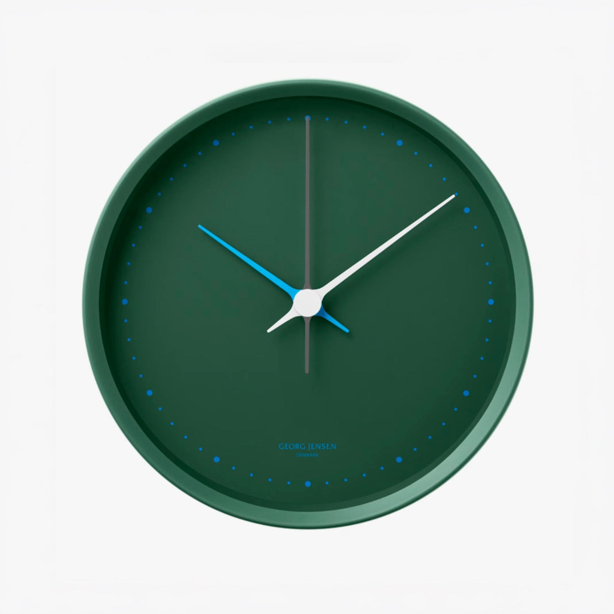 A minimalist round wall clock by Georg Jensen, featuring a dark forest green face and matching green frame, with contrasting blue and white hands and blue minute markers, shown against a plain white background.