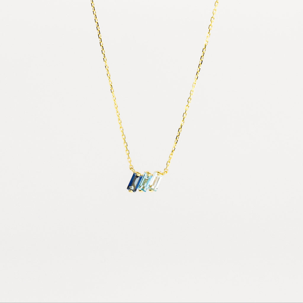 Gold necklace with a blue gemstone pendant on a light gray background
