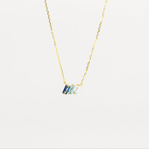 Gold necklace with a blue gemstone pendant on a light gray background