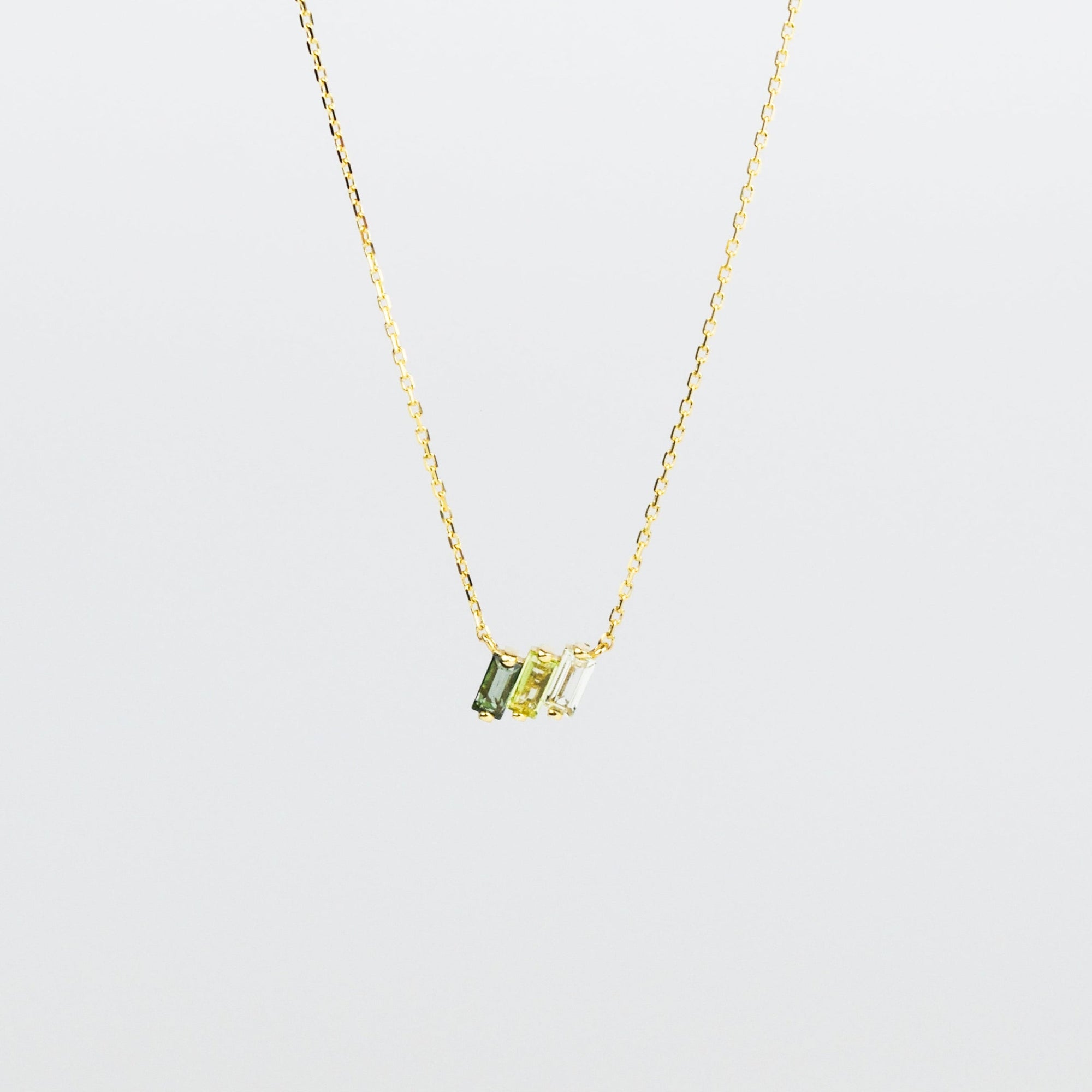 Gold necklace with green gemstones on a light gray background