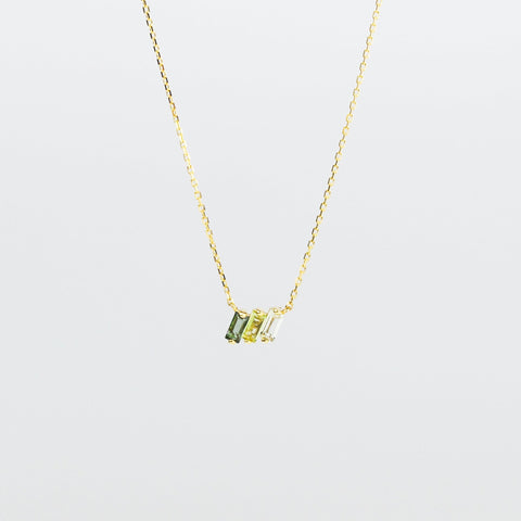 Gold necklace with green gemstones on a light gray background