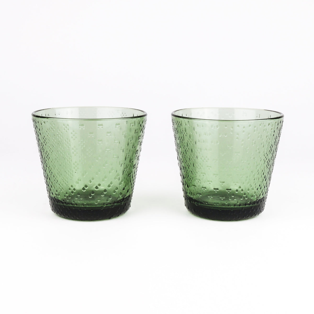 A pair of textured green glass tumblers with a hammered pattern and dark green bases, set against a plain white background.