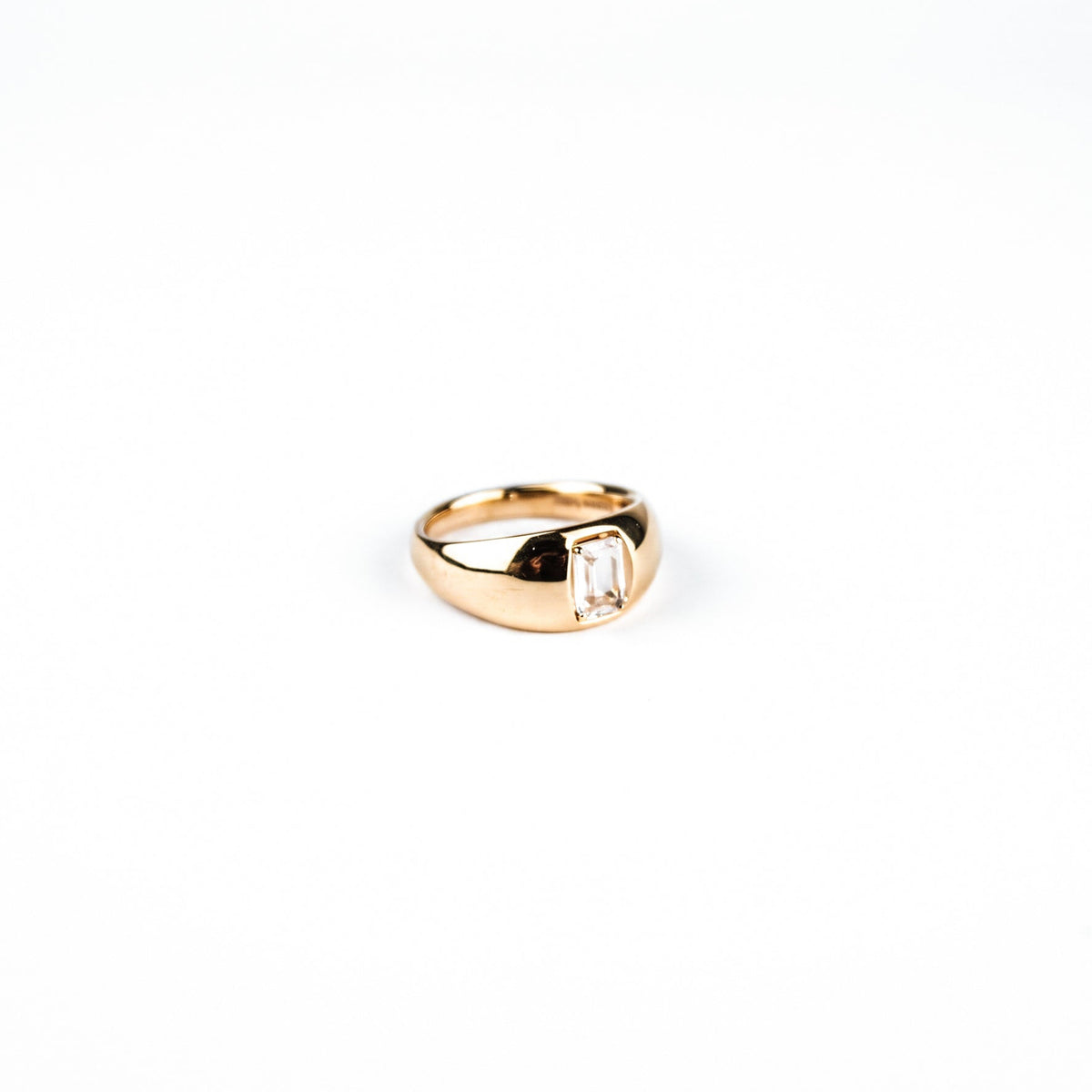 A gold signet-style ring with a rectangular clear baguette-cut gemstone, shown on a plain white background.