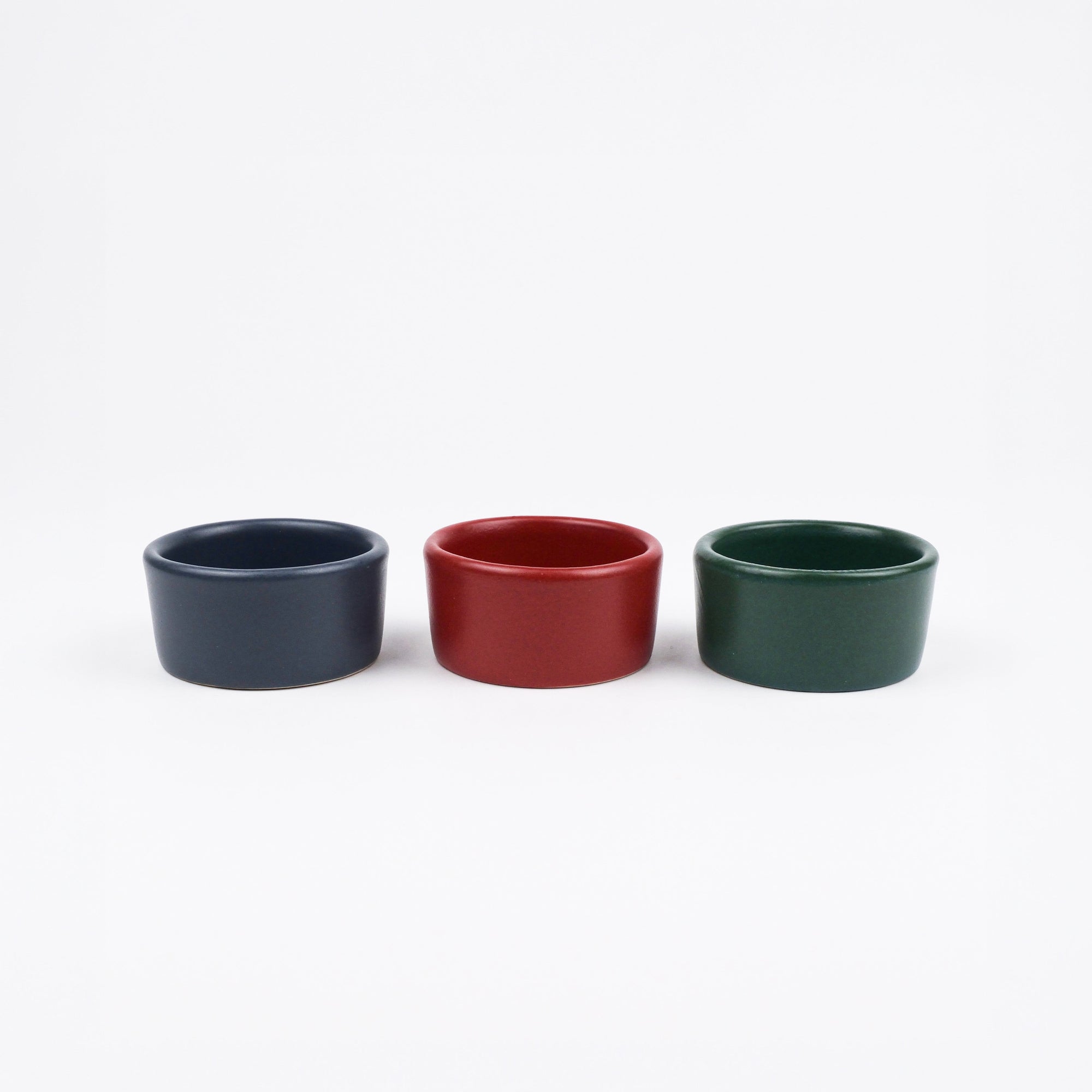 Three small ceramic ramekins in blue, red, and green on a white background