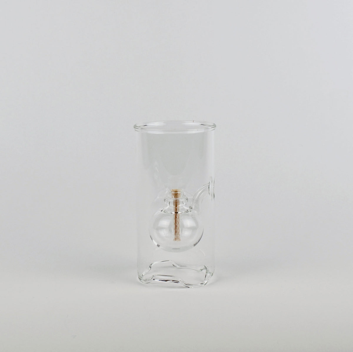 A clear glass double-walled cup with a small central gold-toned accent, photographed against a seamless light gray studio background.