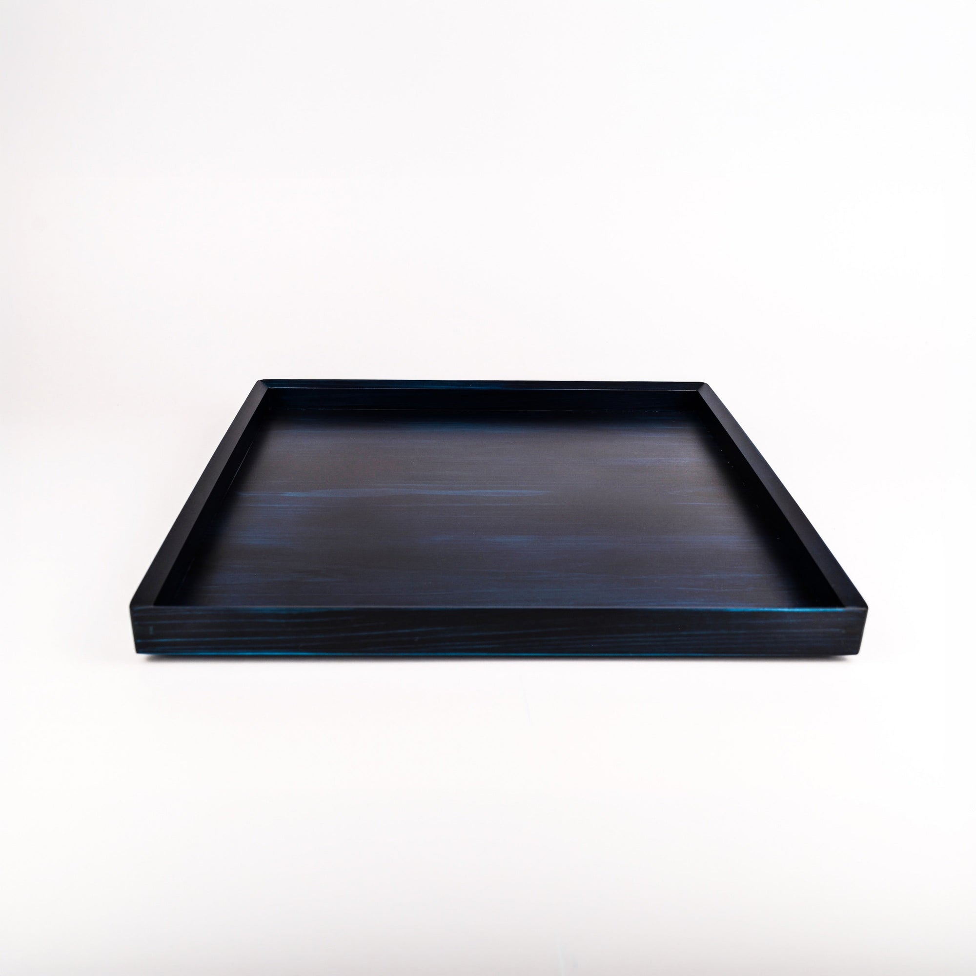 A square indigo blue wooden tray with a smooth, slightly glossy finish, photographed from a direct overhead angle on a seamless white background.