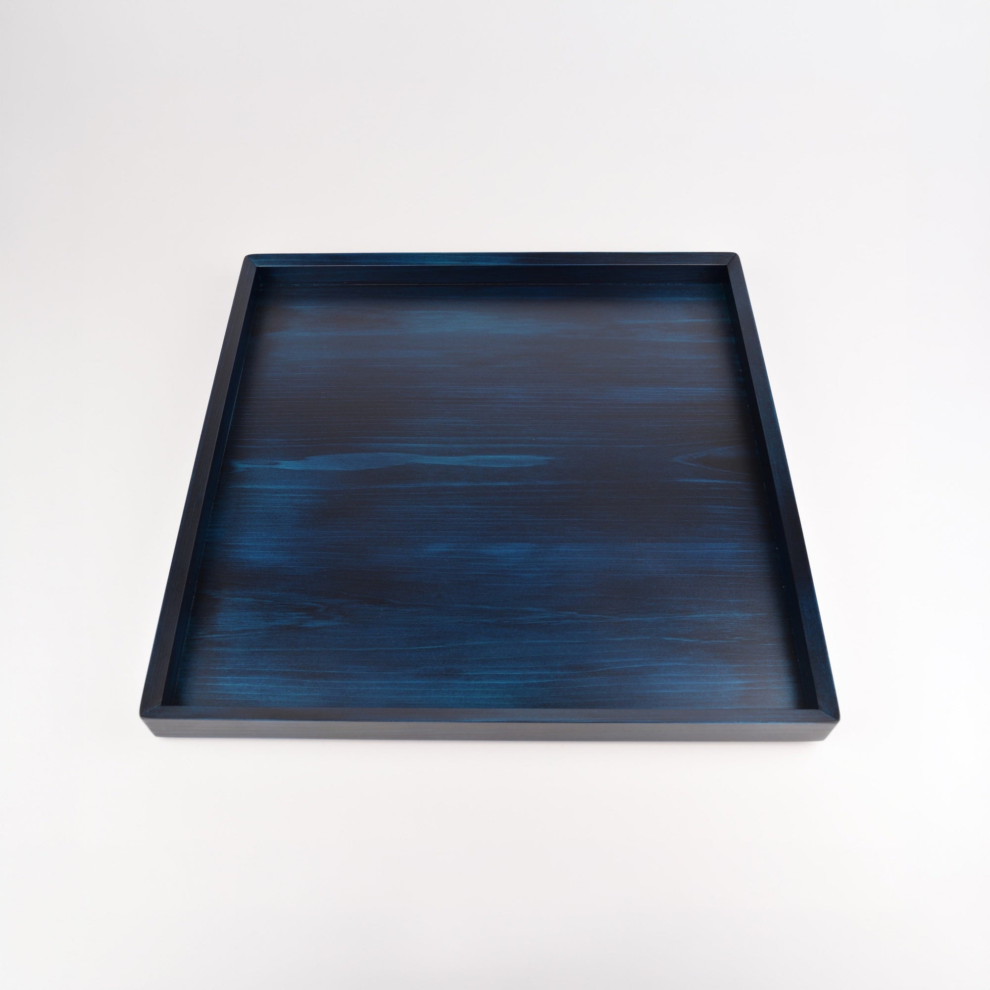 A square wooden tray with a dark blue and black watercolor-like textured finish, photographed from a top-down perspective on a clean white background.