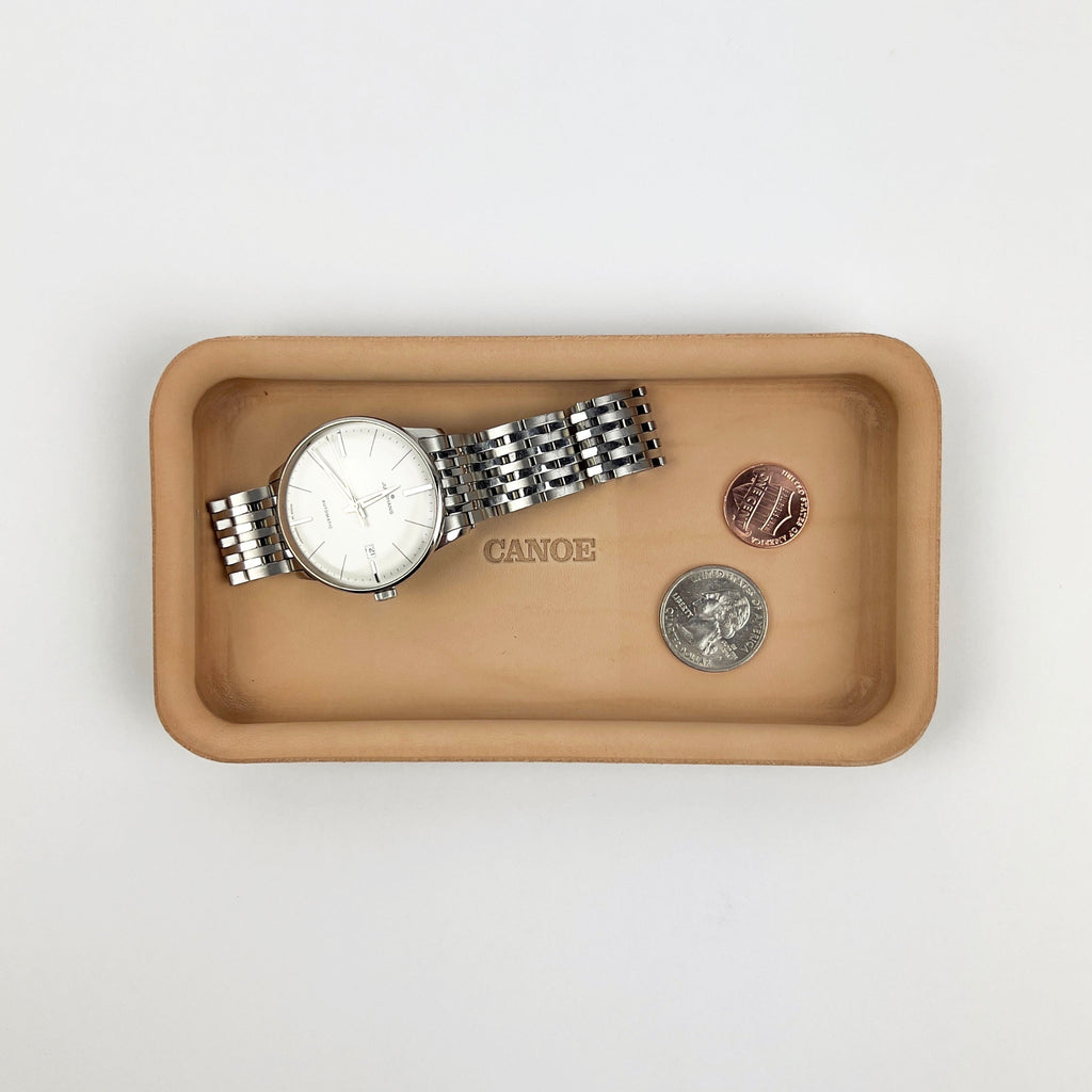 Beige tray with a watch and coins on a light gray background