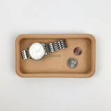 Beige tray with a watch and coins on a light gray background