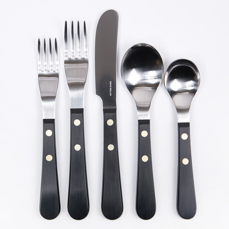 A set of David Mellor Provencal flatware, including a salad fork, dinner fork, dinner knife, soup spoon, and teaspoon with black acetal handles and brass rivets.