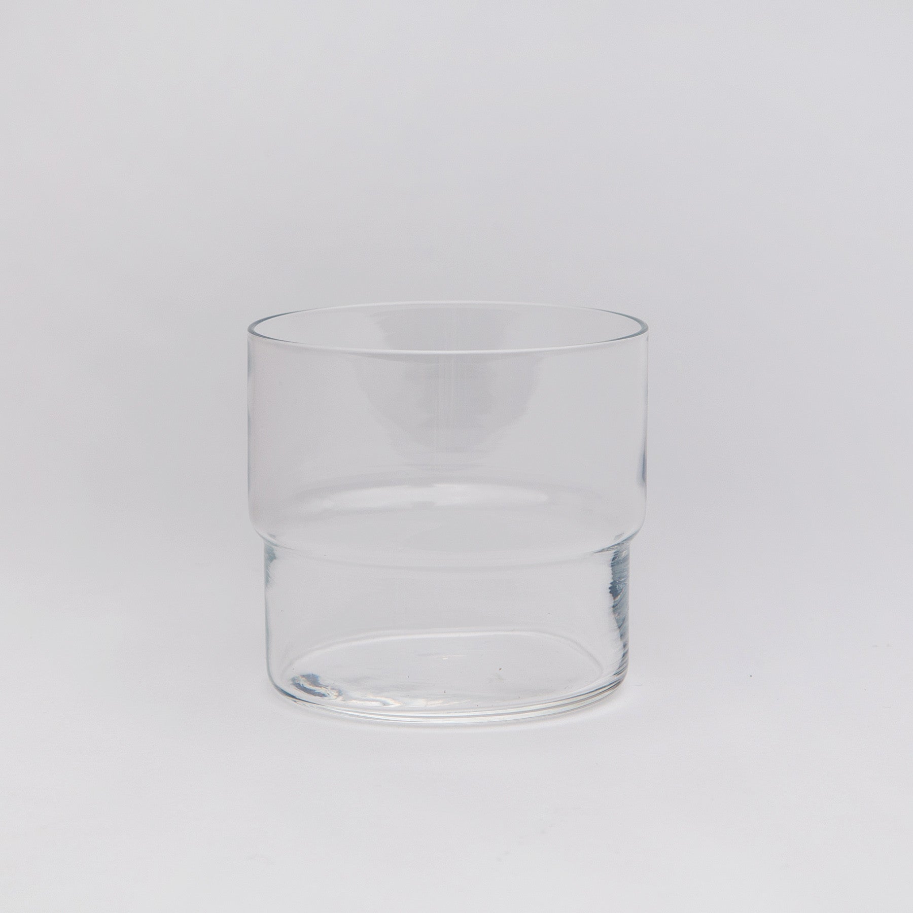 A clear stacking tumbler glass on a white background.