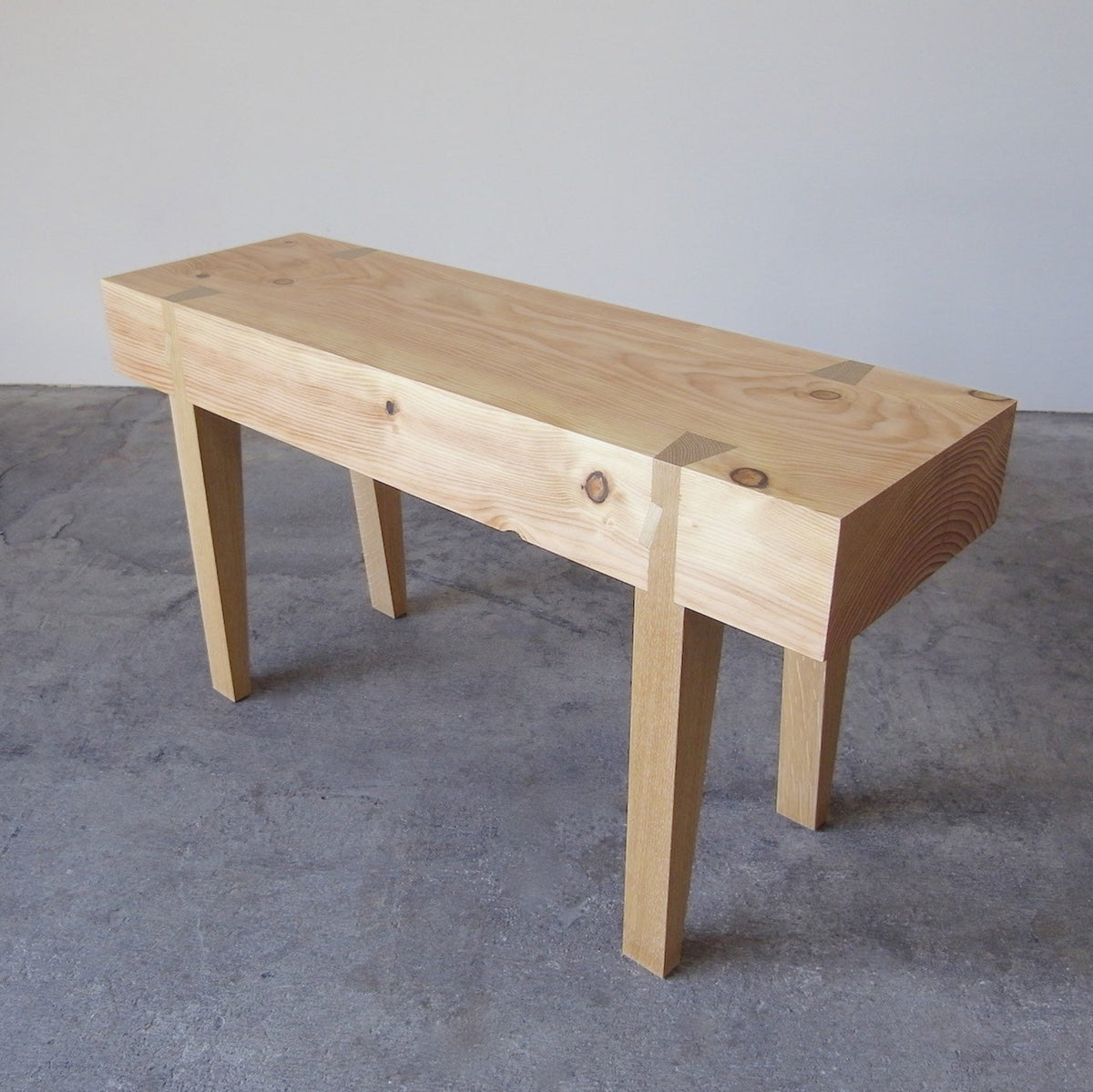 A small scaled handcrafted bench with a wooden seat and legs, displayed against a simple background.