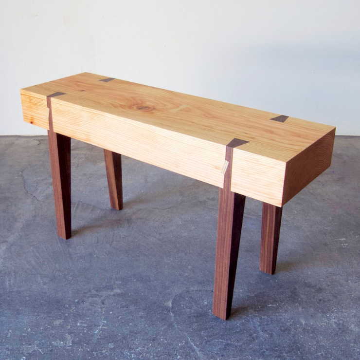 A small scaled handcrafted bench with a wooden seat and legs, displayed against a simple background.