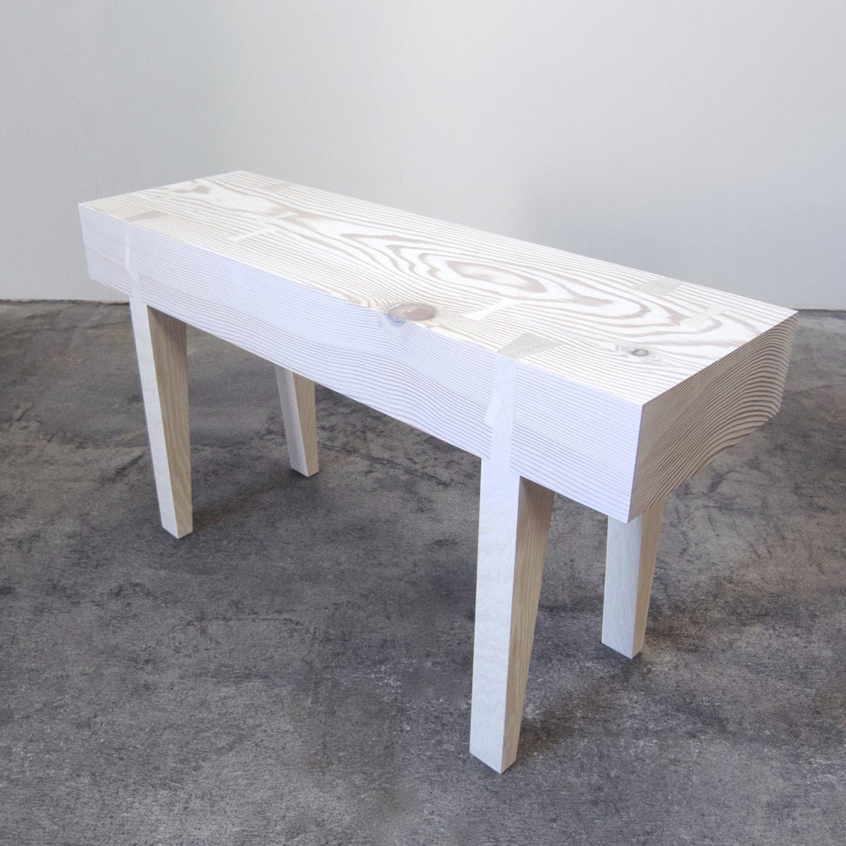 A small scaled handcrafted bench with a wooden seat and legs, displayed against a simple background.
